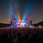 Outdoor music festival at night in La Mancha region, Spain. Large crowd watching a rock concert on a big stage with colorf...