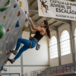 Young female rock climber scaling an indoor climbing wall, Spanish sports hall, athletic gear, focused expression, style. ...